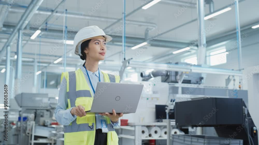 Portrait of an Asian Female Engineer in Hard Hat Standing and Using Laptop Computer at Electronic Manufacturing Factory. Technician Thinking About Daily Tasks and Working on Development Data.