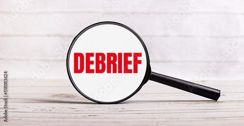 The magnifying glass stands vertically on a light background with the text DEBRIEF