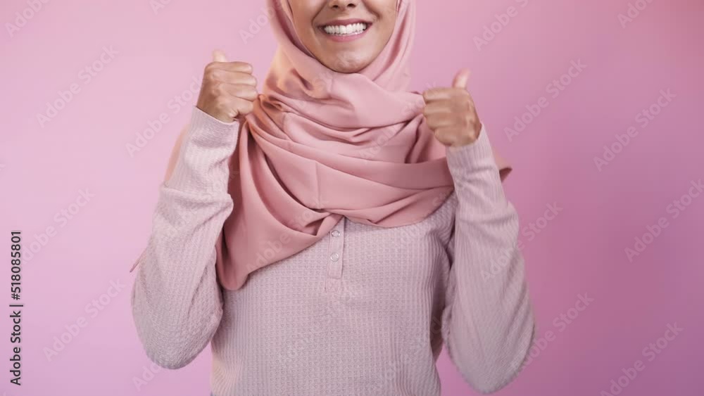Celebrating woman. Success joy. Goal achievement. Excited overjoyed happy toothy smile female winner in hijab showing thumbs up on pink studio background. Celebrating woman. Success joy. Goal achievement. Excited overjoyed happy toothy smile female winner in hijab showing thumbs up on pink studio background.