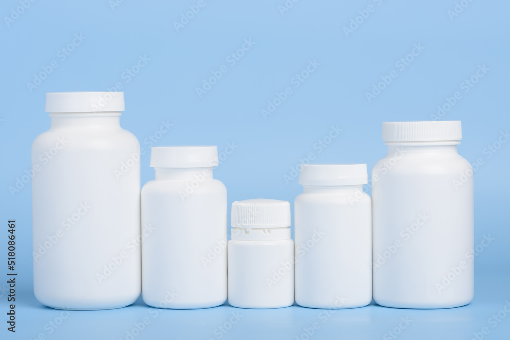 Different sizes of blank white plastic bottles of medicine pills or supplements in a row on blue background Different sizes of blank white plastic bottles of medicine pills or supplements in a row on blue background
