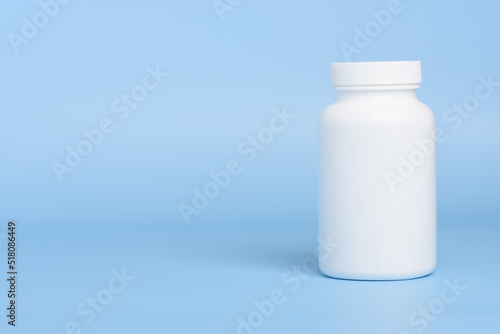 One white blank plastic medical pill or supplement bottle on blue background with copy-space