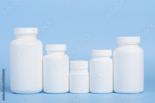 Different sizes of blank white plastic bottles of medicine pills or supplements in a row on blue background
