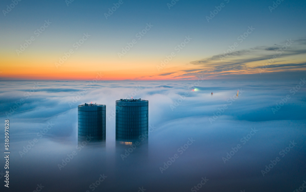 Skyscraper rooftop over the clouds at sunrise. Thick fog covers the Riga city, and warm sunlight over the clouds and church tower.