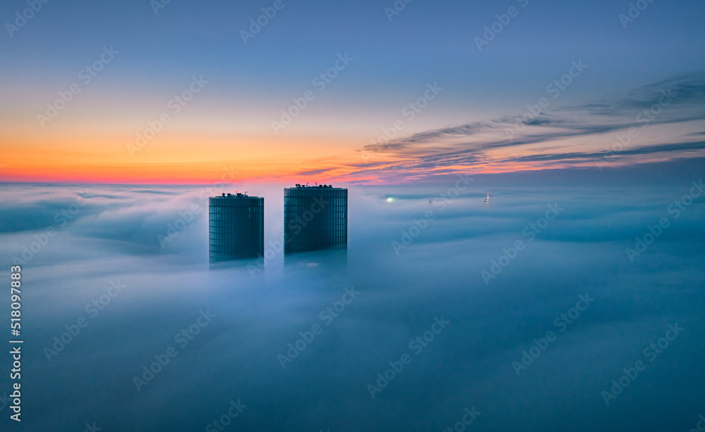 Skyscraper rooftop over the clouds at sunrise. Thick fog covers the Riga city, and warm sunlight over the clouds and church tower.