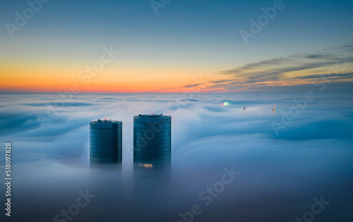 Skyscraper rooftop over the clouds at sunrise. Thick fog covers the Riga city, and warm sunlight over the clouds and church tower.