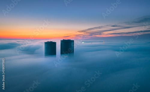 Skyscraper rooftop over the clouds at sunrise. Thick fog covers the Riga city  and warm sunlight over the clouds and church tower.