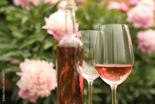 Fototapeta Naklejka Na Ścianę i Meble -  Glasses and bottle with rose wine against beautiful peonies, closeup. Space for text