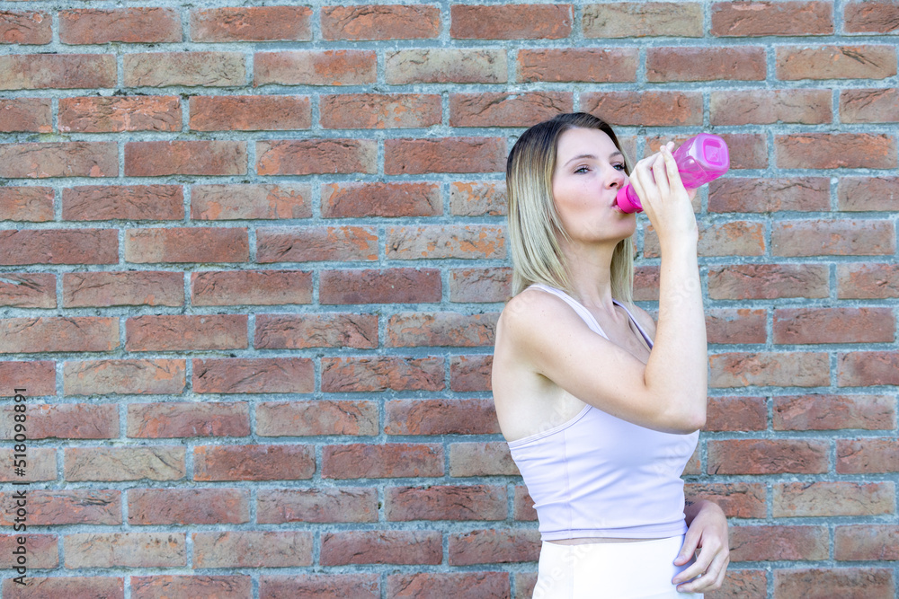 Close up portrait of an attractive young sporty blonde caucasian woman wearing pink sports attire drinking water from a bottle High quality photo Close up portrait of an attractive young sporty blonde caucasian woman wearing pink sports attire drinking water from a bottle High quality photo