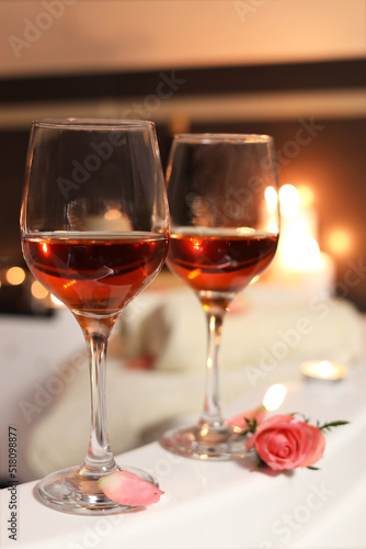 Wine in glasses and rose on edge of bath indoors, closeup. Romantic atmosphere
