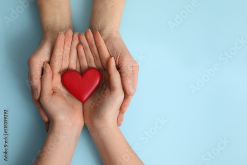 Young and elderly women holding red heart on light blue background  top view. Space for text