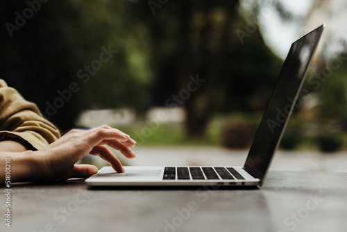 woman's hand on the touchpad of the laptop standing on the grey table on the background of the park