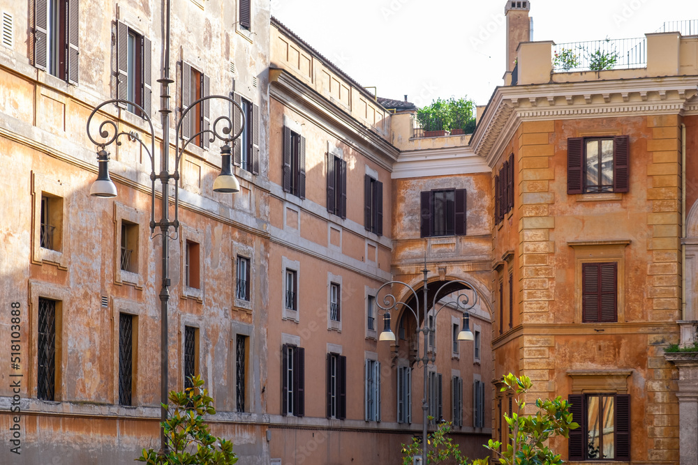 Naklejka premium View of old impressive ancient stone buildings with window shutters and with arched passage. Vintage lantern in the foreground. an impressive historic building in the old city of Rome