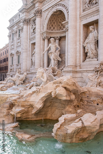 Fotografi Impressive side view of one of the most famous landmarks in the world - Trevi Fountain in Rome in bright sunlight with ancient buildings in background