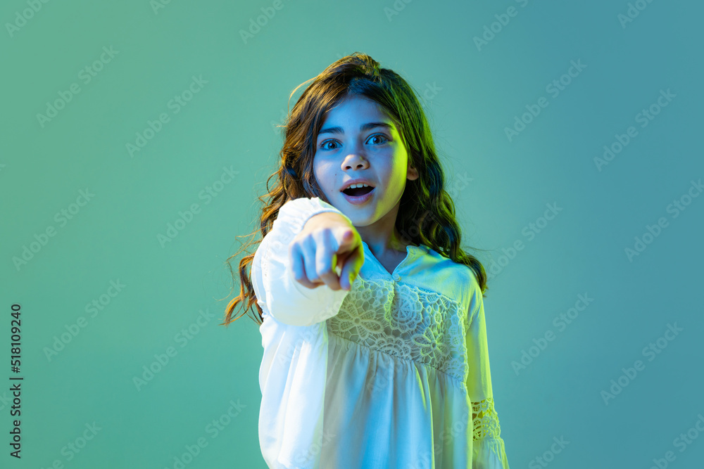 Shocked little girl, kid in casual style clothes isolated over cyan color background in white neon light. Concept of children emotions, fashion, beauty, school and ad Shocked little girl, kid in casual style clothes isolated over cyan color background in white neon light. Concept of children emotions, fashion, beauty, school and ad