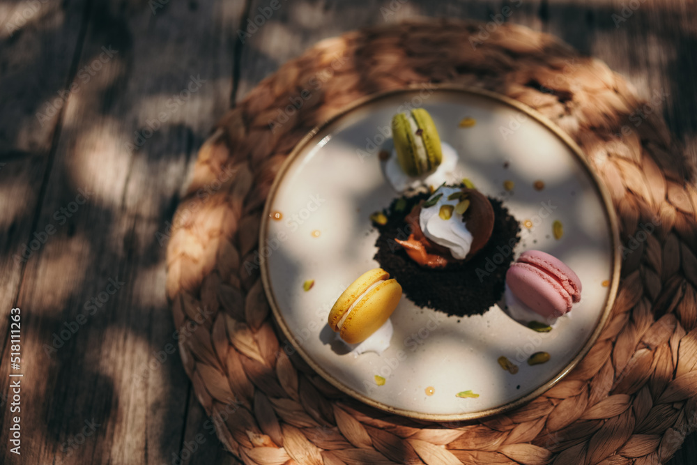 Fototapeta premium Three macaroons served on plate on wooden table in outdoor cafe