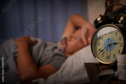 depressed old man and stressed lying in bed from insomnia,focus on the clock