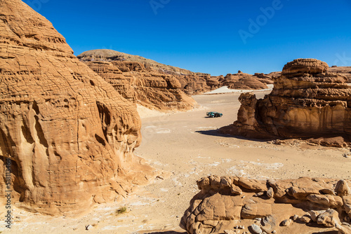 Car in White Canyon in Sinai. Yellow and orange sandstone textured carved mountain, bright blue sky. Egyptian desert landscape. Sinai peninsula, Egypt