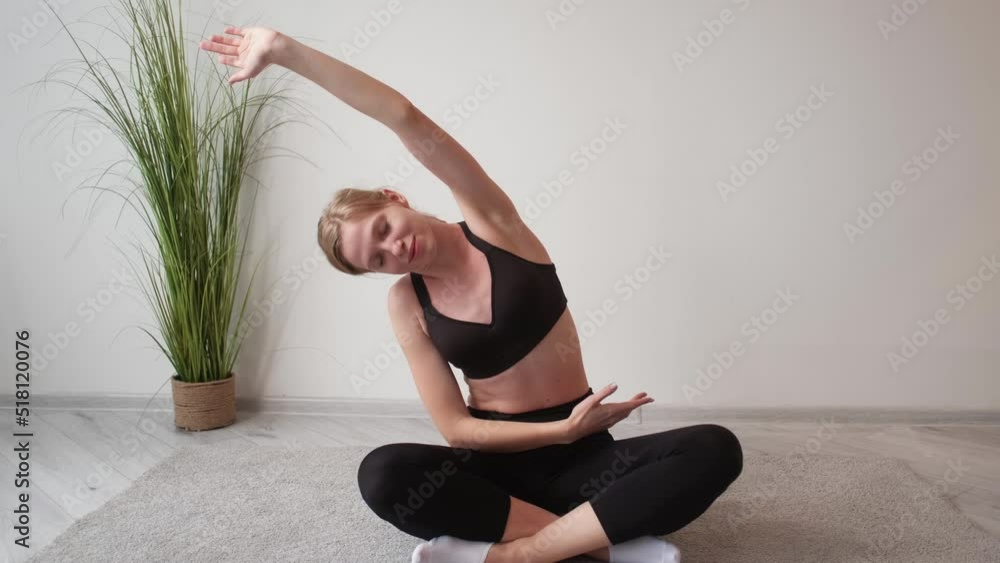 Home pilates. Online yoga class. Indoor fitness training. Relaxed athletic instructor woman stretching back muscles sitting cross-legged at light interior with free space. Home pilates. Online yoga class. Indoor fitness training. Relaxed athletic instructor woman stretching back muscles sitting cross-legged at light interior with free space.