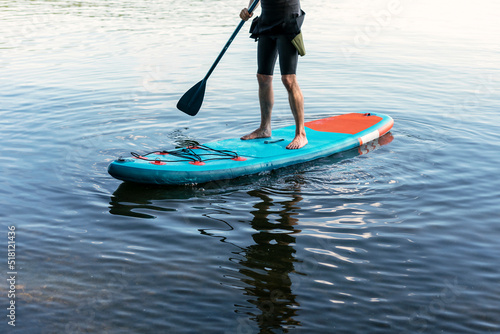 Fototapeta Naklejka Na Ścianę i Meble -  Man faceless in thermo suit paddling stand up paddleboard blue SUP on the water lake with paddle male legs active lifestyle summer activities copy space