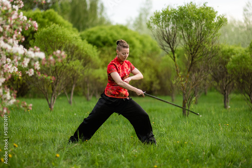 Asian woman with sword training with tai chi in the park, chinese martial arts, healthy lifestyle concept.