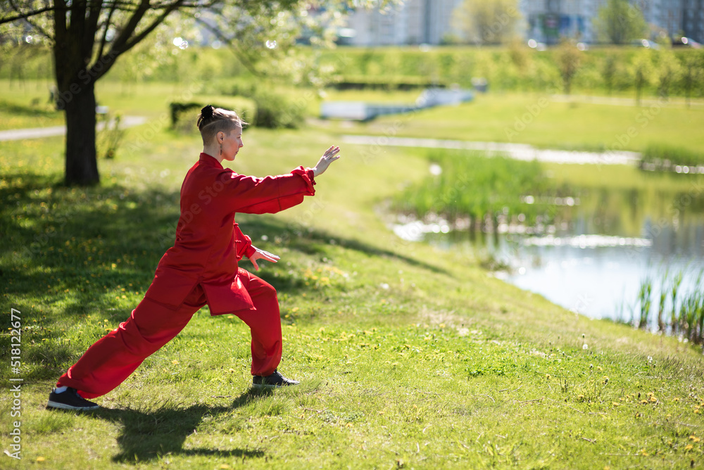Asian woman in red kimano practicing taijiquan outdoors, chinese martial arts, healthy lifestyle concept.