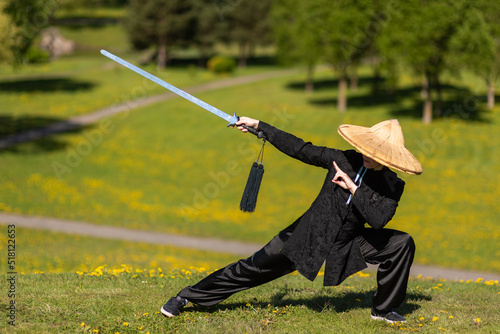 Asian woman with sword practicing taijiquan outdoors, chinese martial arts, healthy lifestyle concept. photo