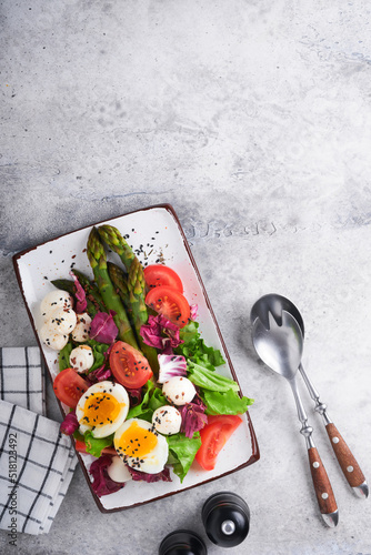 sparagus, tomato, lettuce, mozzarella, black sesame, flax, oil olive salad and soft boiled egg on rectangular ceramic plate on grey concrete table background. Healthy diet food concept. Top view. photo