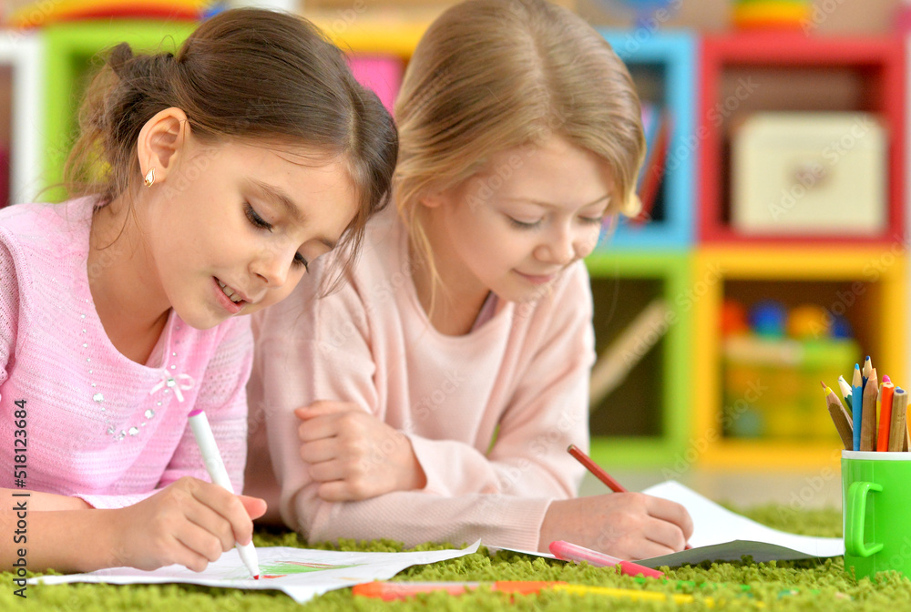 Two cute little girls drawing with pencils while lying on floor Two cute little girls drawing with pencils while lying on floor