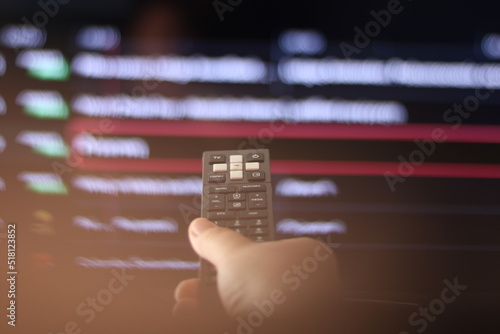 Hand with a remote control, in the background is a TV with a list of channels.