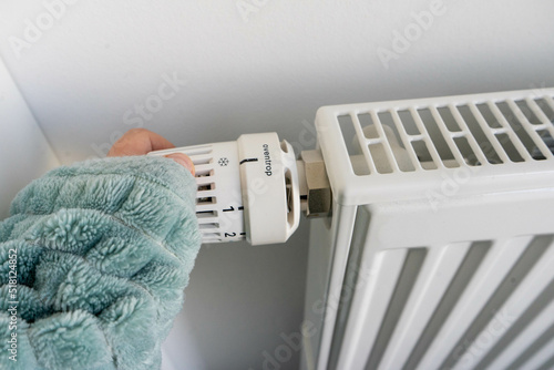 Person mit decke schaltet Thermostat auf Heizung herunter, um Energie zu sparen. photo