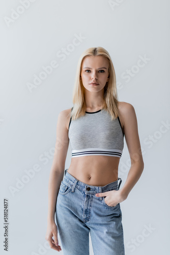 Pretty blonde woman in jeans and top standing isolated on grey.