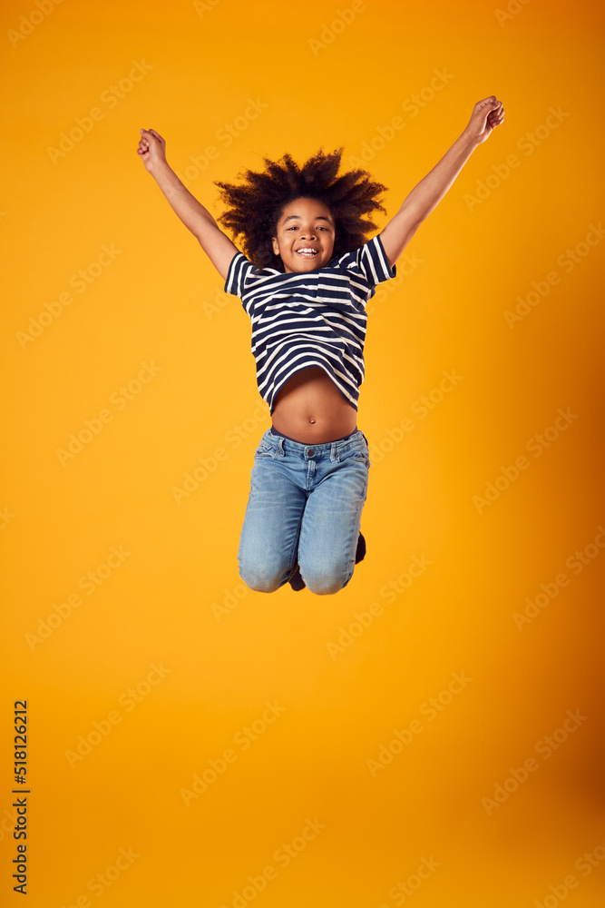 Studio Shot Of Energetic Boy Jumping In The Air With Outstretched Arms Against Yellow Background Studio Shot Of Energetic Boy Jumping In The Air With Outstretched Arms Against Yellow Background