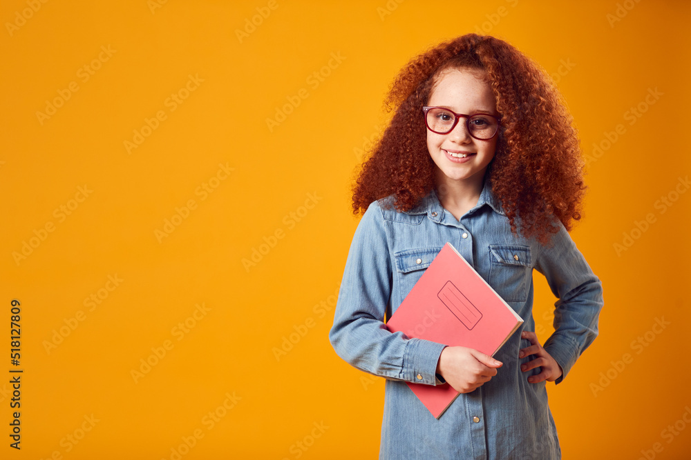 Fototapeta premium Studio Portrait Of Young Girl With School Exercise Book Wearing Glasses Against Yellow Background