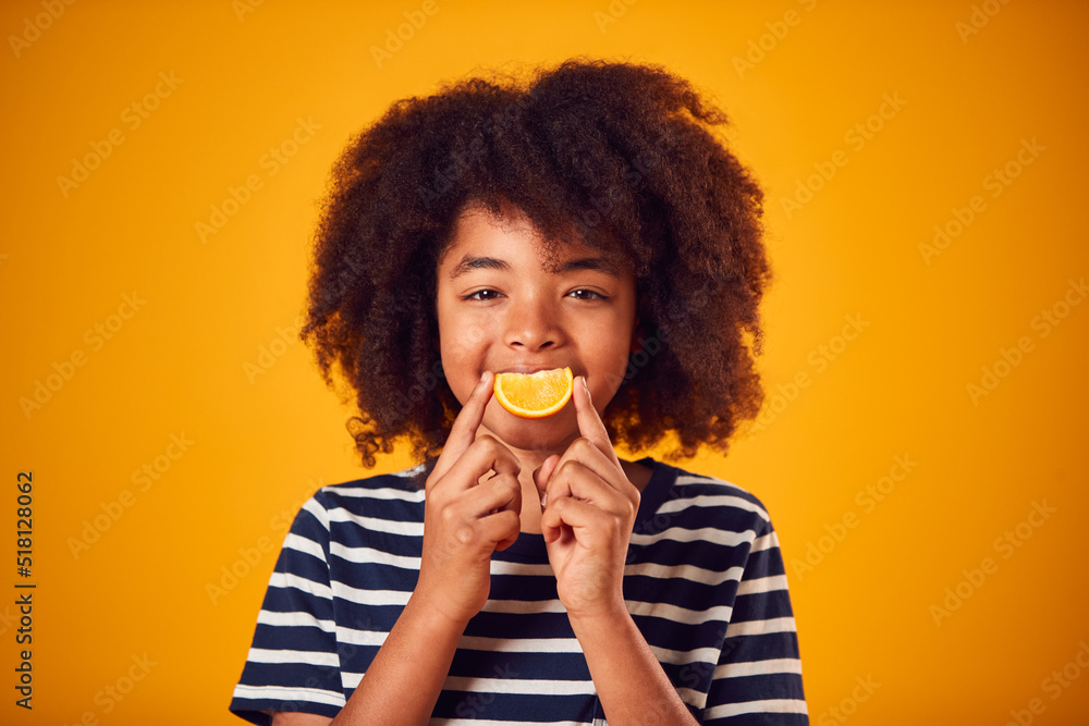 Studio Portrait Of Boy Holding Orange For Smiling Mouth Against Yellow Background Studio Portrait Of Boy Holding Orange For Smiling Mouth Against Yellow Background