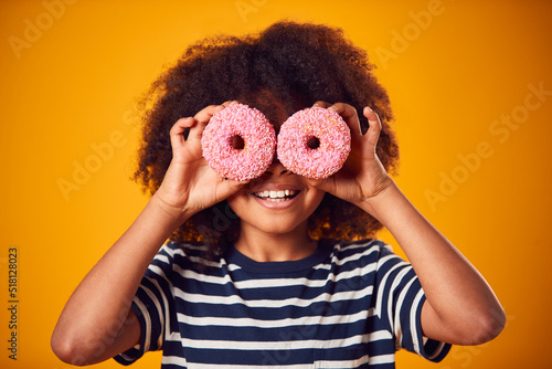 Obraz na plátne Studio Portrait Of Boy Holding Two Donuts In Front Of Eyes Against Yellow Backgr