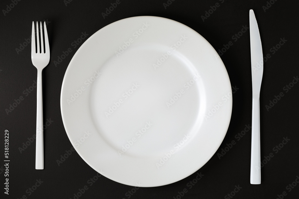 White plate and cutlery on the black background.