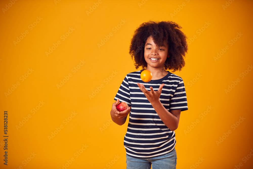 Studio Portrait Of Boy Juggling Apple And Orange Against Yellow Background