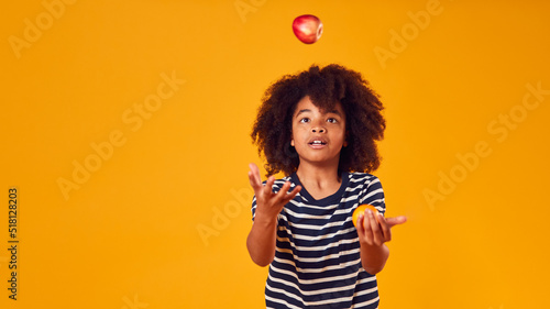 Studio Portrait Of Boy Juggling Apple And Orange Against Yellow Background