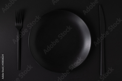 Black plate and cutlery on the black background.