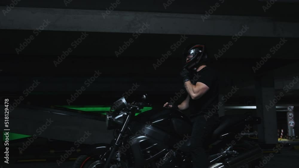A man sitting on a motorcycle takes off his helmet in underground parking garage, slow motion A man sitting on a motorcycle takes off his helmet in underground parking garage, slow motion