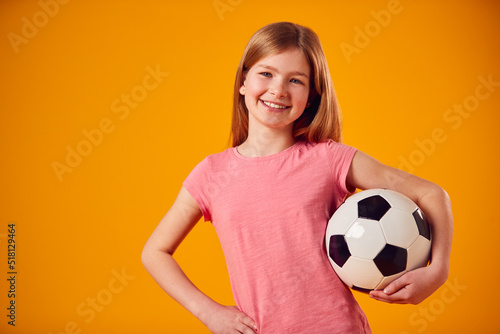 Studio Shot Of Young Girl Holding Soccer Ball Under Arm Against Yellow Background © Monkey Business