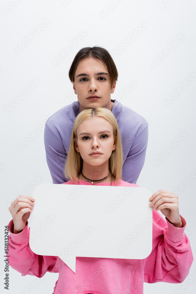 Brunette man looking at camera near girlfriend with white speech bubble isolated on grey. Brunette man looking at camera near girlfriend with white speech bubble isolated on grey.