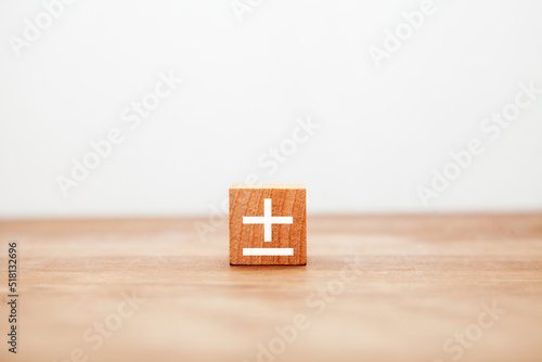 プラスマイナスの記号。±。木製ブロックに書かれている。白い文字。木製テーブルの背景。 photo