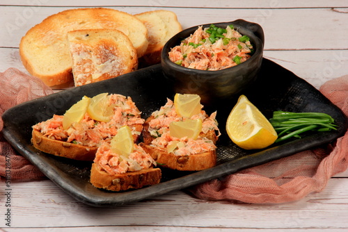 Sandwiches with chopped salmon pate on a black clay plate, light wooden board background