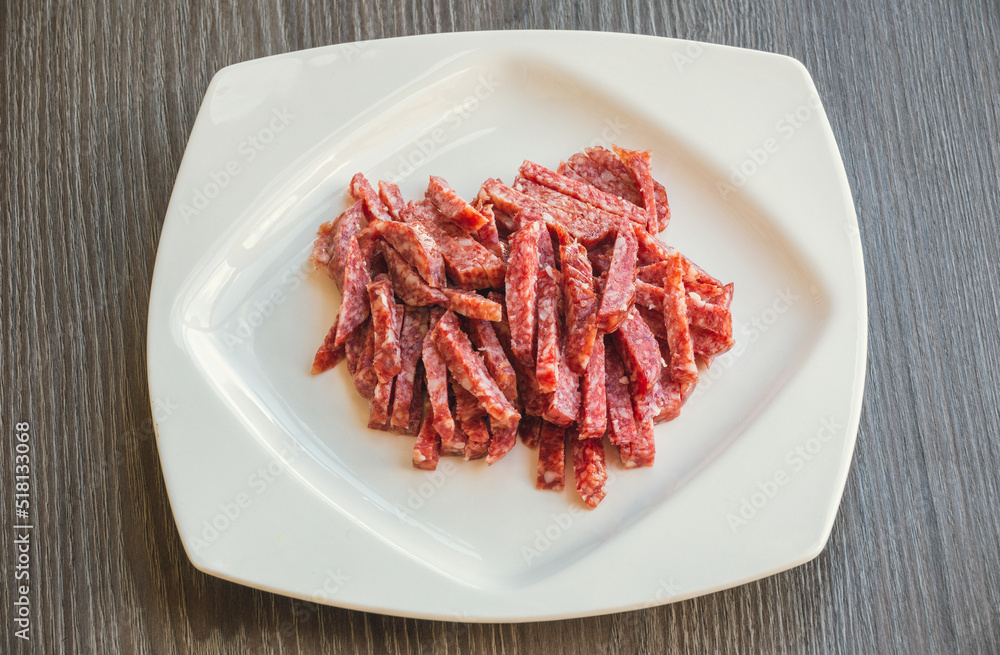 Lots of Spanish Serrano ham and Spanish sausage, festive, Iberian pork loin on a white platter. Smoked sausage cut into small slices in a white plate close-up selective focus.  Meat products.