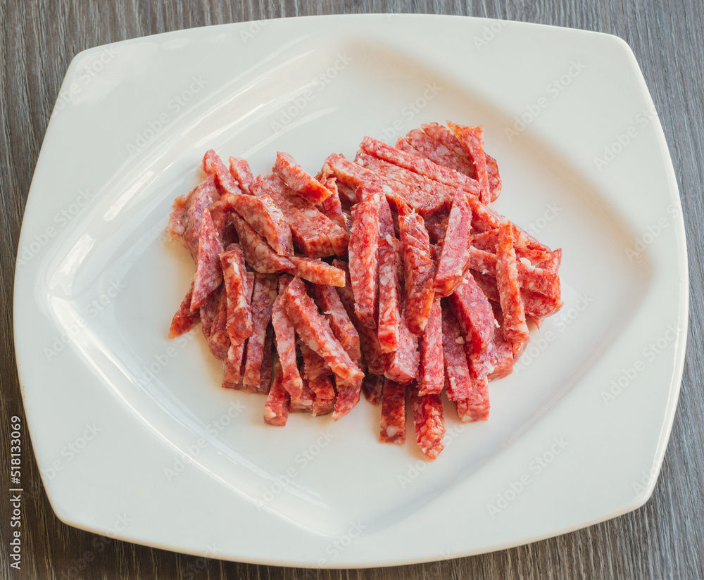 Lots of Spanish Serrano ham and Spanish sausage, festive, Iberian pork loin on a white platter. Smoked sausage cut into small slices in a white plate close-up selective focus.  Meat products.