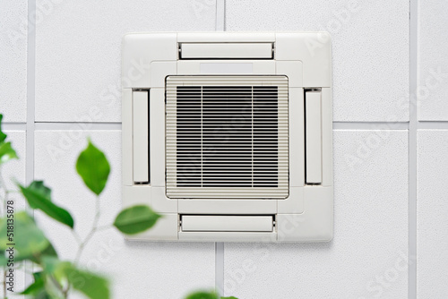 Cassette Air Conditioner on ceiling in modern light office or apartment with green ficus plant leaves. Indoor air quality and clean filters concept photo