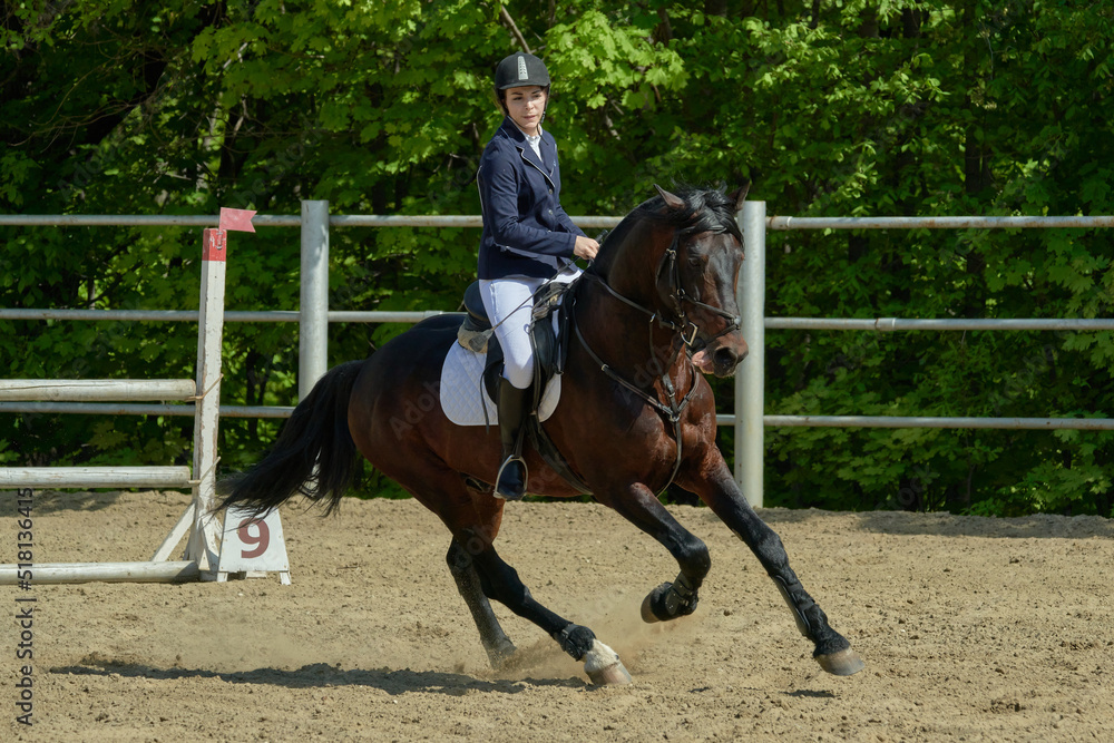 A young woman performs a sports race on a horse on a sunny summer day.