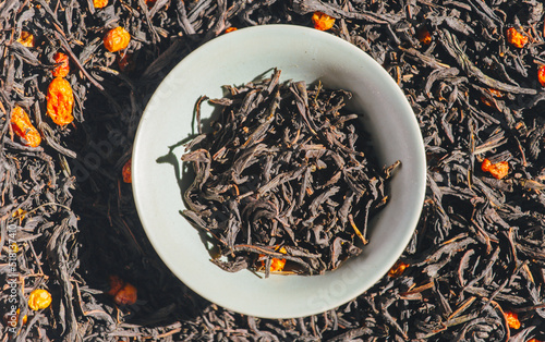 Green tea with berries in a bowl on the background of scattered tea. Ivan tea with sea buckthorn in a bowl background texture. Dried tea leaves and berries background. Chamerion angustifolium.  photo