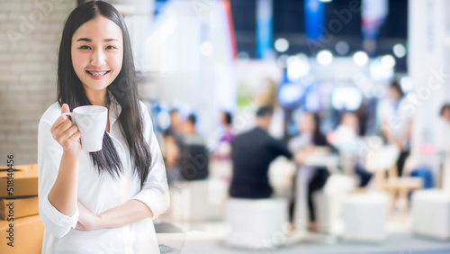 Happy young Asian woman standing at office of her business online shopping with blur people background